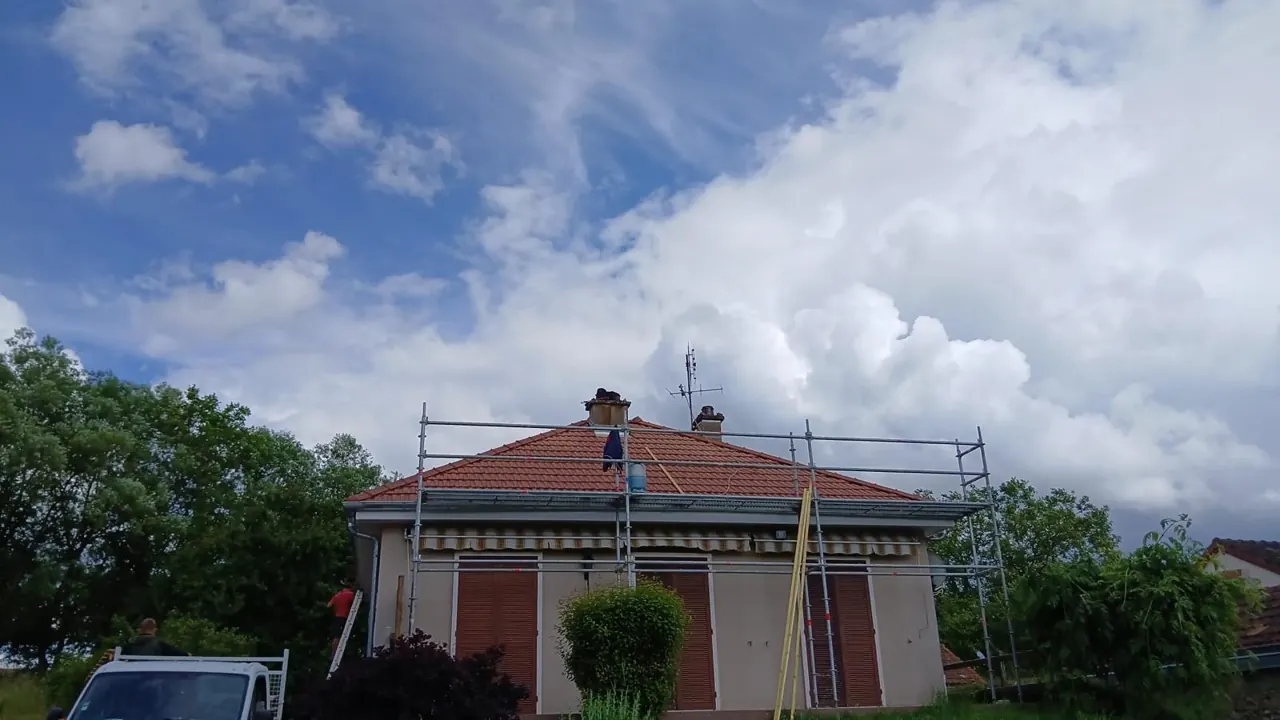 Couvreur sur une toiture en tuiles pendant une rénovation, maison entourée d'un échafaudage