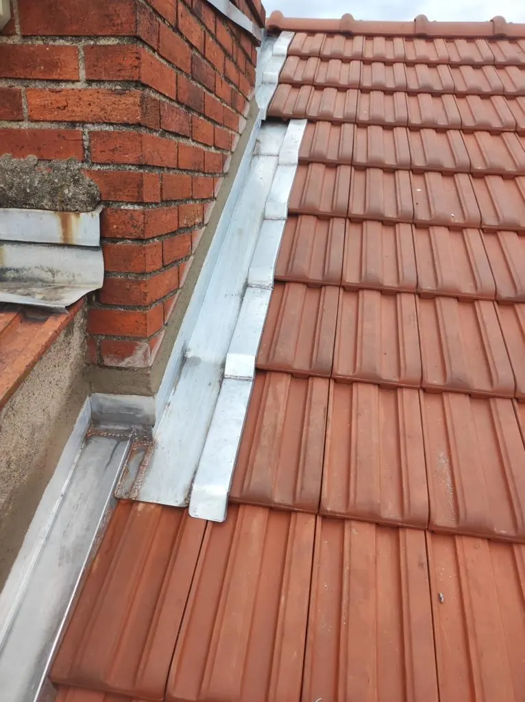 Solin en zinc entre une cheminée en brique et la couverture en tuiles